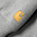 Carhartt WIP Hooded Chase Sweat em Grey Heather com detalhes em dourado. Foto de detalhe do logo bordado na manga.